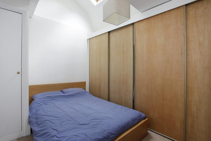 Bedroom with sliding-door birch wardrobe, double bed dressed in blue linen, and small skylight above the bed — fitted into the third-floor mansard space.